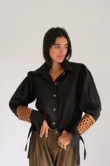 Camisa de lino color naranja, con mangas largas abuchonadas, cuello camisero y cierre frontal con botones. Presenta un diseño único con detalle calado en los puños.