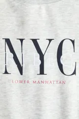 Buzo de cuello redondo con diseño estampado frontal con texto NYC y Lower Manhattan. Presenta hombros caídos, mangas largas y terminaciones acanaladas en puños y ruedo.