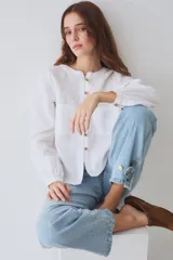 Blusa de lino color blanco, con cuello redondo, manga larga y cierre frontal con botones de madera. Presenta dos bolsillos frontales tipo parche con costuras a la vista.