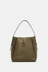 Bolso tipo saca de gran tamaño en color verde militar, confeccionado en material efecto gamuza. Presenta un diseño estructurado con pespuntes decorativos, una anilla metálica dorada en la parte frontal y un asa de hombro ajustable. Cuenta con cierre de botón imantado y bolsillo interior con cremallera.