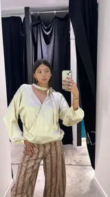 Blusa de satén color beige, con diseño reversible que permite usar el escote pronunciado hacia el frente o hacia la espalda. Presenta mangas largas abullonadas con puños elásticos y un lazo integrado en el cuello para anudar.