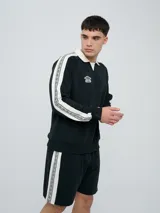 Buzo deportivo Umbro modelo Mixtape, color negro con cuello polo blanco y franjas blancas en las mangas con logo de la marca. Cuenta con puños y cintura elastizados.