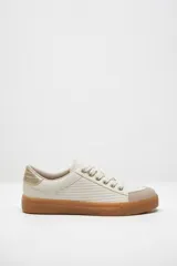 Zapatillas color marfil con detalles dorados en el talón y ojales metálicos. Suela de goma caramelo y cordones beige.