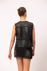 Pollera de jean negro con efecto de lavado localizado, terminación desflecada en el ruedo, tachas cuadradas en la cintura, apliques de alfileres de gancho en el bolsillo y ojalillos metálicos decorativos en la parte inferior.