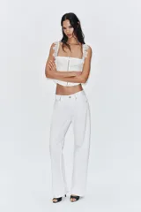 Top corsetero blanco con escote cuadrado y tirantes anchos con volados de encaje. Presenta costuras marcadas y cierre frontal con ganchos metálicos.