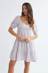 Vestido corto de algodón con estampado de cuadros vichy en color lila y blanco, escote corazón, mangas cortas abullonadas y falda escalonada con volantes.