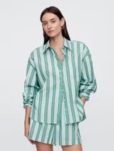 Camisa de corte oversize confeccionada en popelina, con diseño de rayas verticales en tonos verde y blanco. Presenta cuello clásico, cierre frontal con botones y bolsillo en el pecho.