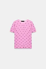 Top de punto fino color rosado, con cuello redondo, manga corta y estampado de lazos morados distribuidos en un patrón de rombos.