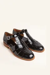 Sandalia cerrada tipo pescador de cuero negro charol, con tira en T y hebilla ajustable en el tobillo. Posee suela y taco bajo de madera.