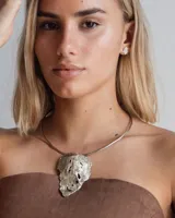 Gargantilla rígida de metal dorado con dije central de diseño orgánico y textura irregular. El diseño permite múltiples usos, incluyendo la opción de utilizar la gargantilla sola o con el dije.