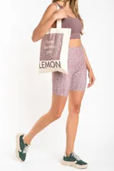 Bolsa tipo tote bag color crudo, con tiras de hombro, confeccionada en 100% algodón. Presenta un diseño gráfico frontal con estampado en tonos morados que incluye texto con las palabras "fitness, wellness, gym" y la marca "LEMON" en la parte inferior.