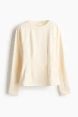 Buzo de felpa color beige con cuello redondo acanalado, mangas largas raglán y costuras moldeadoras en la cintura que crean una silueta entallada.