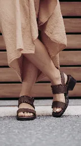 Sandalia de cuero color marrón, con taco bajo de madera, tiras anchas en el empeine y detalle de cordones entrelazados en el lateral. Cuenta con tira ajustable con hebilla en el talón.