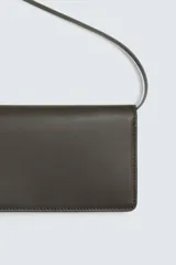 Cartera tipo bandolera de piel color marrón oscuro, con solapa y cierre a presión. Incluye seis ranuras para tarjetas, una ranura para billetes y un monedero interior con cierre de cremallera. Posee un asa de hombro ajustable y extraíble.