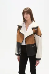 Chaqueta estilo aviador o biker, con paneles de color marrón (simil gamuza), negro (simil cuero acolchado) y blanco (simil borrego/sherpa). Presenta cuello solapa ancho forrado en blanco, detalles de hebillas negras en los hombros y cierres metálicos en la parte delantera.