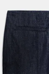 Pantalón capri de tiro medio confeccionado en denim de algodón. Presenta bolsillos de vivo en el delantero, cierre frontal con cremallera, botón y ganchos metálicos, y aberturas laterales en el bajo.