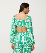 Blusa cropped blanca con estampado de motivos verdes, escote corazón con lazo, mangas largas abullonadas y confeccionada en tricolina.