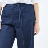 Pantalón jean de tiro bajo con corte ancho y pierna recta. Presenta un diseño de cinco bolsillos, cierre frontal y un cordón ajustable en la cintura.