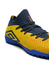 Championes de fútbol 5 Umbro modelo Ignis TF, con diseño de corte medio en tejido elástico color azul marino y cuerpo texturizado en color amarillo. Presenta suela de goma con tapones pequeños para césped sintético y logo de la marca en el lateral.