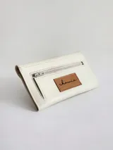 Billetera de cuero vacuno color crudo con textura granulada. Presenta un diseño tipo sobre con cierre de broche y un detalle decorativo de espiga bordado en cuero color suela en la solapa frontal.