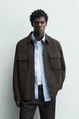 Sobrecamisa relaxed fit color beige con tejido elástico, cuello solapa, manga larga con puños abotonados, bolsillos de plastrón con solapa en el pecho, bolsillos laterales de vivo en la cadera y cierre frontal de botones.