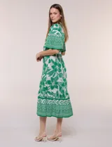 Vestido midi de estilo bohemio en color verde y blanco, con estampa floral, escote en V, cierre frontal con botones, mangas cortas amplias, cintura ajustable con lazo y volado en el bajo.