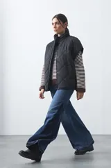 Chaleco acolchado de nylon negro con diseño capitoneado de rombos, cuello alto y cierre frontal con botones a presión.