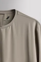 Camiseta deportiva de manga larga Zara Athleticz, de corte regular fit y color marrón topo. Confeccionada en tejido técnico elástico de secado rápido, cuenta con cuello redondo y detalle de logo estampado en el bajo.