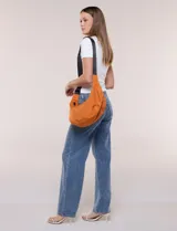 Cartera bandolera de lona naranja en forma de medialuna, con correa ajustable negra y cierre principal.