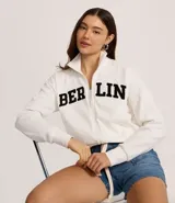 Chaqueta deportiva blanca con cierre frontal, cuello alto y puños ajustados. Presenta la inscripción "BERLIN" en letras negras y gruesas en el pecho.