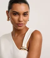 Blusa de punto color crudo, con escote en V y mangas asimétricas: un lado con manga corta y otro musculosa. Tiene un adorno metálico dorado en el bretel.