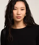 Suéter ajustado de punto color crema, con cuello redondo y mangas largas con botones metálicos en los puños. Confeccionado con viscosa sostenible.