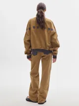Pantalón jean de tiro alto y corte pinzado, con perneras de caída suelta y levemente anchas en el bajo. Posee pasador con hebilla en la parte trasera.