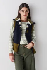 Chaleco de lana con cierre frontal completo, cuello alto y diseño bicolor en tonos marrón y celeste. Presenta una combinación de tejido trenzado y acanalado, con un corte asimétrico más largo en la parte posterior y aberturas laterales.