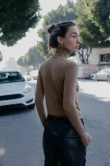 Jersey de punto liso en color beige, con cuello alto y manga larga con detalle de botones metálicos en los puños.
