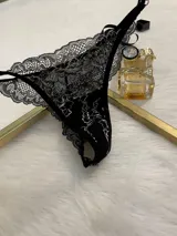 Conjunto de lencería compuesto por bralette triangular y tanga, confeccionado en encaje bitono negro y blanco. El bralette presenta cierre frontal con broche de gancho y breteles regulables. La tanga es de estilo colaless con laterales regulables mediante herrajes metálicos.