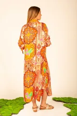 Vestido camisero midi color naranja con estampado floral y paisley. Tiene cuello camisero, mangas largas con puños abotonados, bolsillos laterales y aberturas laterales en el ruedo.