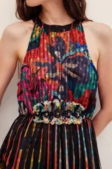 Vestido largo con cuello halter y escote cerrado, con diseño plisado y estampado multicolor con detalles abstractos y florales. Presenta un aplique bordado decorativo en la cintura.