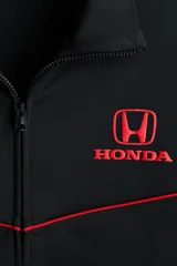 Campera deportiva negra de efecto neopreno con cierre bidireccional, cuello elevado y bolsillos laterales. Presenta detalles de ribetes rojos en el pecho y el logo de Honda bordado en rojo.