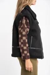 Chaleco estilo gamulán de color negro, con interior y detalles de corderito sintético. Presenta cierre frontal, cuello solapa y bolsillos laterales.