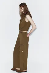 Pantalón cargo de tiro alto en color marrón tostado, con diseño de pernera holgada que se estrecha hacia el tobillo. Presenta bolsillos frontales con cierre de cremallera, bolsillos laterales de plastrón con solapa y botón, y cierre frontal con cremallera y botón.