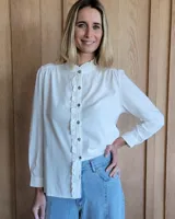 Camisa blanca de manga larga con cuello mao y volantes verticales en el frente.