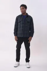 Campera tipo sobrecamisa de franela con diseño a cuadros en tonos beige y marrón. Presenta cuello clásico, cierre frontal con botones, dos bolsillos frontales con solapa y botones en el pecho, y mangas largas con puños abotonados.