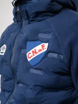 Campera Umbro del Club Nacional de Football, modelo Alpine. Diseño en color azul marino con frente acolchado termosellado, mangas y espalda de tejido polar, capucha integrada y cierre frontal completo. Incluye logo de Umbro y escudo del club en el pecho.