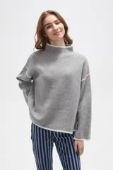 Polera de tejido de punto color negro con detalles de vivos en color beige en el cuello, puños, ruedo y costuras de las mangas. Presenta un diseño holgado con cuello alto y mangas largas.