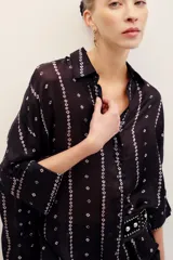 Camisa de seda negra con estampado geométrico de líneas verticales con rombos pequeños en tonos claros, cuello camisero, mangas largas con tajitos en los puños y cierre frontal con botones.