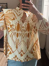 Camisa de lino color crudo con estampado geométrico y tribal en tono tostado, cuello camisero, cierre frontal con botones y mangas largas abullonadas con hombros estructurados.