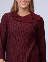 Blusa de tejido piqué con estampado geométrico en tonos negro y bordó. Presenta cuello volcado, mangas tres cuartos y un diseño de ruedo asimétrico.