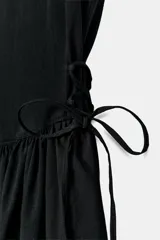 Vestido corto negro confeccionado en 100% algodón, de cuello redondo y mangas cortas. Presenta detalle de lazadas en los laterales de la cintura y falda con vuelo.