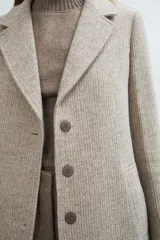 Saco corto entallado de lana fina, con cuello solapa, manga larga y cierre frontal con botones. Presenta un diseño clásico con textura de espiga en tonos tierra.